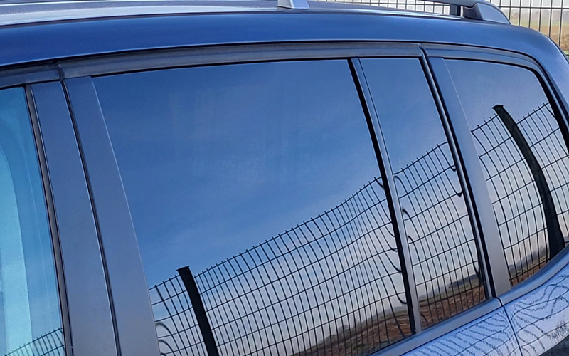 Reflexionen eines Stabmattenzauns auf den Scheiben eines Autos